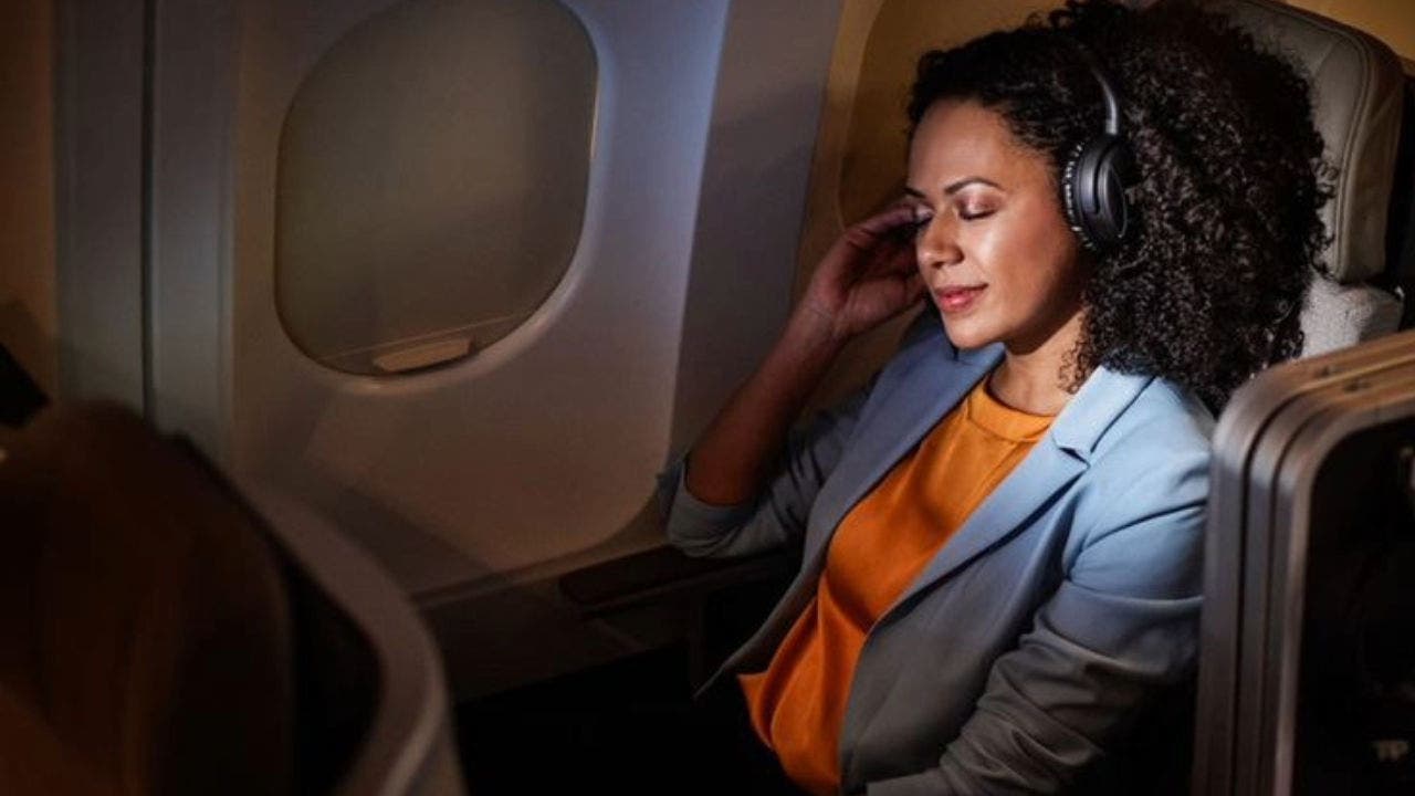 Imagem de uma senhora a bordo de um avião TAP em classe executiva com a luz de ambiente baixa promovendo um ambiente acolhedor enquanto ouve musica através de uns headphones