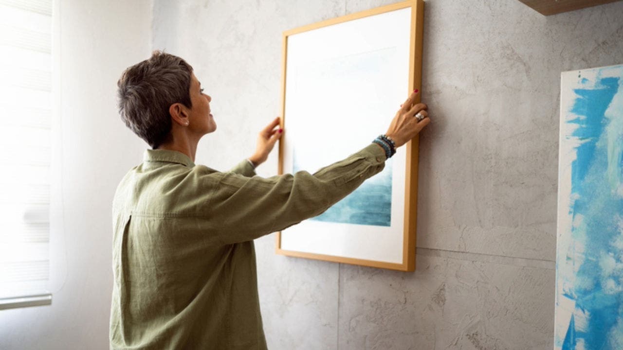 Woman decorating her home with a new painting.